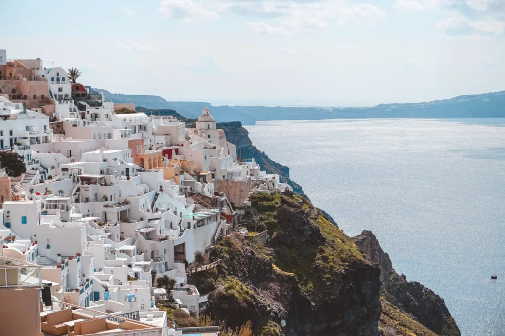 View of Santorini's volcanic landscape and Oia, with its white-washed buildings perching on dramatic cliffs. 