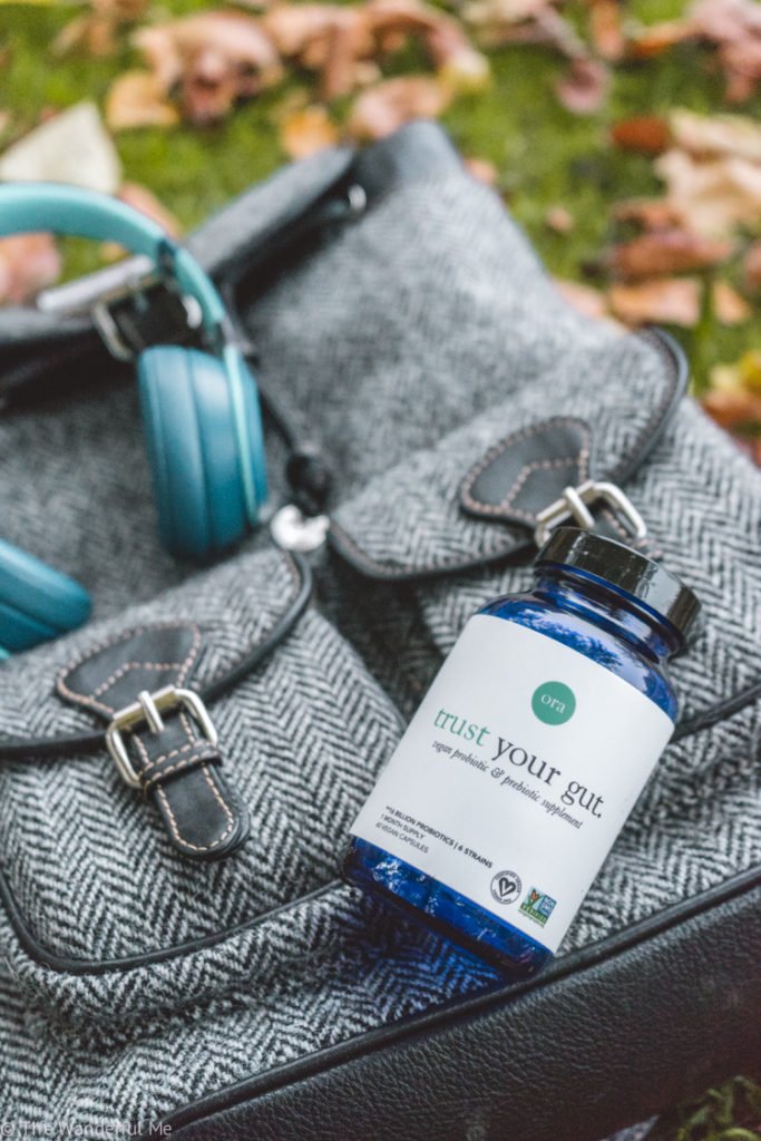 The Trust Your Gut travel probiotics bottle resting on Sophie's backpack with a pair of headphones in the background. 