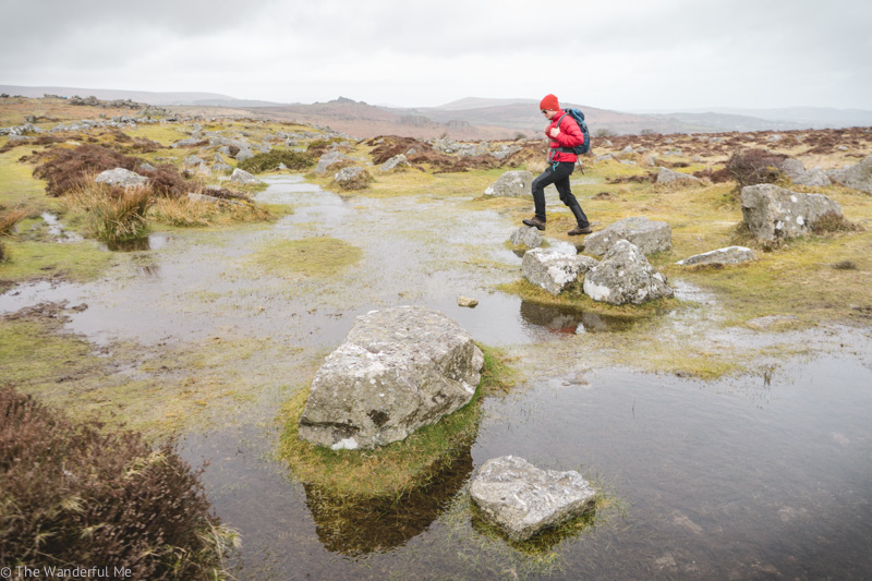 Dan standing on a rock in Dartmoor National Park with water, rocks, and grass all around him. 